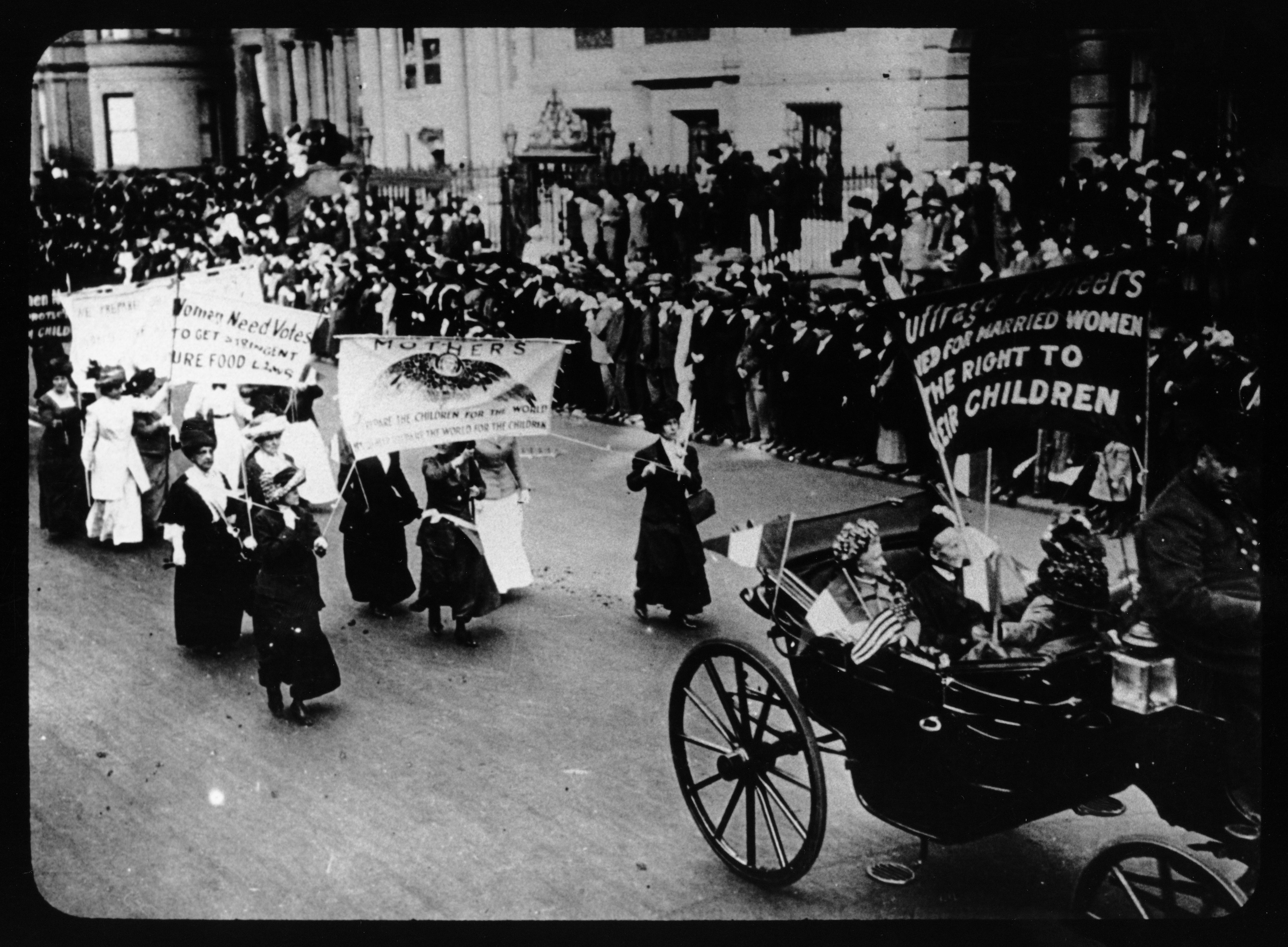 Women in horse-drawn carriage and on foot march in street for voting rights carrying banners PICTURE Kheel Center Kheel Center, Cornell University Library