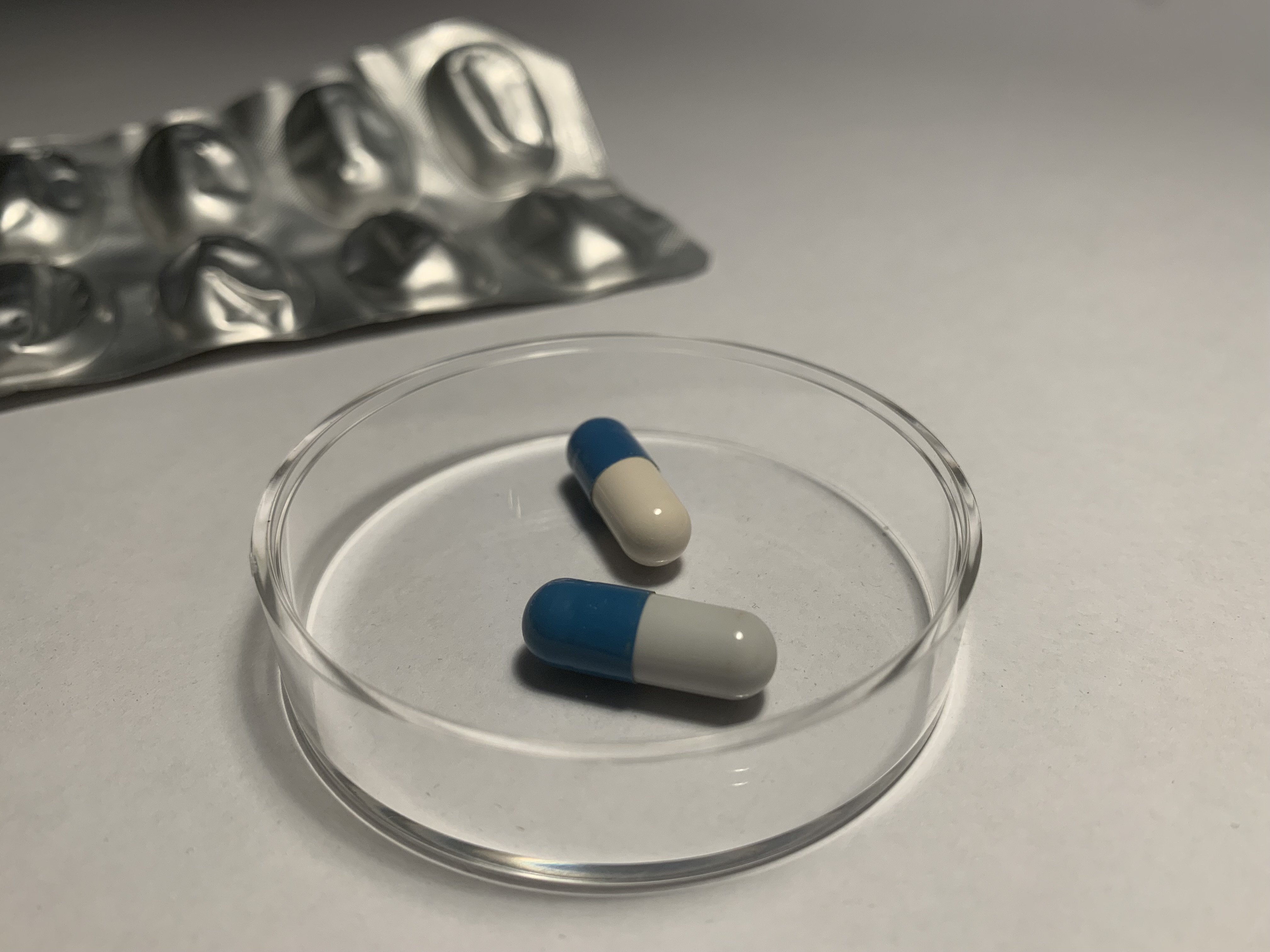 Blå-vita antibiotikakapslar i en petriskål, med en tom bilsterförpackning i bakgrunden. Anton Lundvall